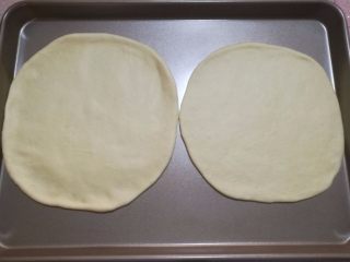 4、鲜虾火腿披萨,4.将面团拿出来排气，平均分成两份，滚圆，盖上保险木松弛15分钟，用擀面杖将面团擀成两个八寸的圆形。用手调整一下，圆形外圈比中间厚一些。