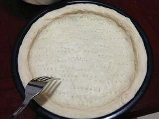 7、【培根菠萝披萨】,把面皮放入披萨盘，整成形状。用叉子叉些小孔。