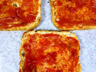 3、全麦核桃吐司披萨,在烤盘上铺上硅油纸，将3片全麦核桃吐司平铺在硅油纸上，表面涂上适量的番茄酱（有披萨酱最好）