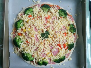 16、西兰花培根披萨,再次撒满芝士碎～多撒点，然后放进预热好的烤箱，中层，上下火180℃烤20分钟