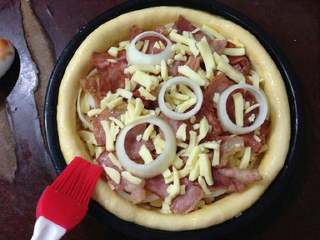 10、培根洋葱披萨,上面再撒些芝士起丝和洋葱圈,把剩余的培根也都放上。皮边刷一层蛋液。
