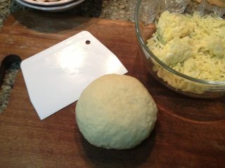 4、肉香满溢披萨,往面团中间塞入软化好的黄油。继续推、搓面团。为了使面团上劲,可以摔打、折叠揉面团。直至面团表面光滑。