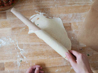 5、土耳其披萨,在工作台上撒好面粉，将面球揉成大圆，约0.5厘米厚。放到烘焙纸上。