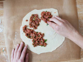 6、土耳其披萨,将羊肉混合我薄薄地抹到面皮上，用指尖轻轻压下。将披萨连烘焙纸一起放入烤箱中，小心地将其放到热好的烤盘中。烤5-8分钟，或直至披萨稍微起泡，且边缘变棕。重复操作，直至用完剩余的面团和馅料。