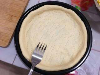 10、虾球玉米披萨,把擀好的面皮放入，做成披萨皮的形状，用叉子叉一些孔子。