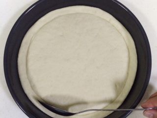 6、培根口蘑田园披萨,把擀好的面饼放入披萨盘内，用手按压面皮，边缘挤出一圈圆边，用汤匙按压出饼皮边缘一圆的轮廓，这样使轮廓比较明显些。