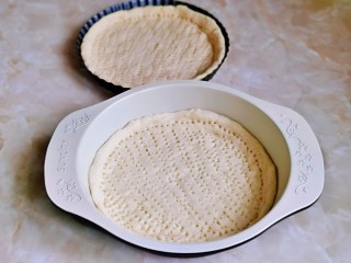 6、虾仁培根披萨,取一块面团，用擀面杖擀出圆饼，与自己的披萨盘一样大小就可以，用食品叉扎出不规则的洞洞眼。