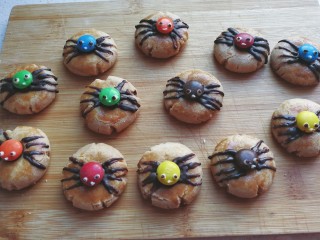 12、万圣节~蜘蛛饼干,最后再把少许白巧克力放在小勺子中隔热水融化,用牙签粗头沾上白巧克力点上蜘蛛的眼睛和嘴巴,再沾点黑巧克力点成黑色眼珠,呆萌可爱的小蜘蛛就做好啦!