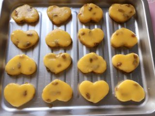 11、葡萄干奶酥,把饼坯摆放在烤盘里，并在表面刷一层薄薄的蛋黄液，放入预热好的烤箱中层，上下火180度，烤18分钟，表面金黄色即可。