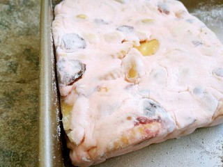 14、草莓味雪花酥,取一只方盘撒一些奶粉将雪花酥整形放在烤盘的一角