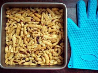 10、蔓越莓沙琪玛,将拌好的坯条倒入方形不粘活底模具内，带上隔热硅胶手套，趁热压紧