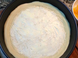 13、HomeMake榴莲披萨（8寸）,在饼皮上均匀的抹上软化好的奶油奶酪。最后用叉子在面皮上戳好洞。