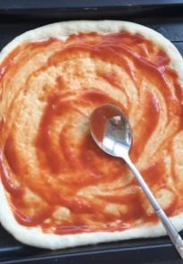 9、夏威夷披萨,将整形好的饼皮平铺，挤上披萨酱并用勺子的背面推开。