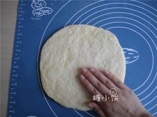 6、烟熏风味BBQ烤鸡肉披萨,在面板上撒多一点玉米面防粘，放上第一步松弛好的面团，用双手从圆心往外抹面团，抻成圆饼状。如图其中一只手的位置就是像这样，由圆心处向外抹。两只手一起，边抹边把面饼转圈这样各个方向都比较均匀，期间可以补些玉米面防粘。