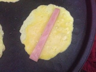 2、鸡蛋火腿卷,锅里刷一层油。用勺子舀一勺鸡蛋糊摊在锅里。上面放一条火腿条