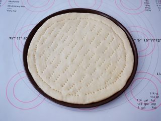 6、杂蔬火腿肠披萨,把面团取出按压排气，擀成跟披萨盘一样大小的圆形，放入披萨盘，用叉子在饼皮上叉些小洞