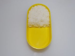 2、卡通面包超人便当「10」,取适量米饭放入便当盒一半，压实备用。