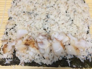 11、鳕鱼肉松寿司,把拌好的米饭铺在海苔上铺平，最好用勺子轻轻压一下，最下边一头放入一排鱼肉块