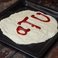 2、培根披萨,在饼上面挤上番茄酱，用勺子抹均匀。