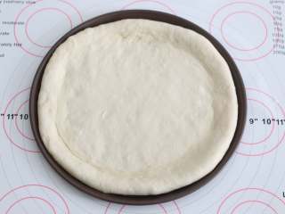 3、自制培根披萨,用擀面杖将面团擀成一个与披萨盘盘底一样大小的饼底，把饼皮铺进去。