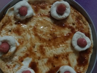 3、披萨做法,发酵好的面团分两份，大份擀成圆形放披萨盘里，小份分成6等份包上火腿放周围，披萨饼用叉子戳小孔后刷上披萨酱