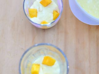 8、芒果冻芝士,把刚才做好的冻芝士糊倒入加了饼底的杯中，倒入一部分，加入几个芒果粒。 