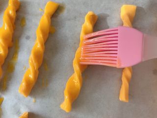 10、#宝宝辅食#南瓜磨牙棒 10M+,烤盘铺油纸，卷好的饼干放在油纸上，蛋黄打散后滴入柠檬汁去腥，用刷子均匀刷在饼干表面；