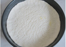 3、台湾香肠什蔬批萨,将圆片放入盘内，用手整理好，用叉子在面片上扎许多的小眼