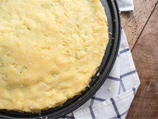 3、意大利式南瓜菠菜玉米饼披萨,把温度降低至190摄氏度；披萨盘上喷油防粘；碗中放入Trader Joe粗磨玉米粉 ，融化的椰子油 ，混合均匀；把玉米粉混合物倒在披萨盘上，整成0.8厘米的厚度，覆盖住披萨盘底。