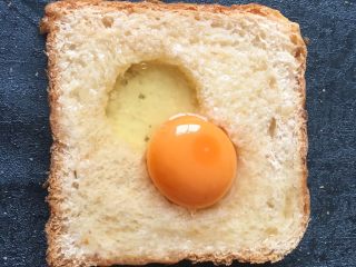 6、早餐+鸡蛋芝士土司面包,将鸡蛋打入洞中多余的蛋清淋在周边面包上