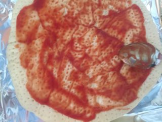 1、火腿虾仁蘑菇披萨,从冰箱拿出之前制作好的饼皮不用解冻，涂一层番茄沙司