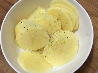 2、火腿芝士烤土豆片,放入碗中，调入盐和黑椒粉用手抓匀备用。