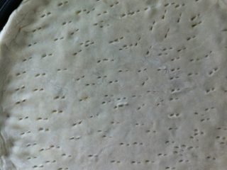 4、饼铛披萨,把发好的面的揉成面团，擀成圆形面饼，边缘用手捏成厚一点的边，放在冰场上，用叉子在面饼上叉几下