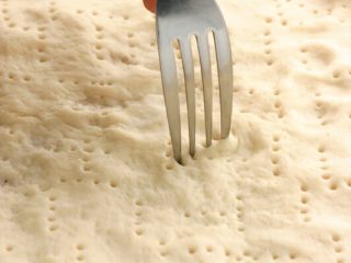 2、素食披萨,工作台上撒上少许高筋面粉,将作法6面团沾少许高筋面粉,用手压成圆饼状,用叉子在面皮戳小洞即可。