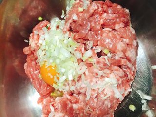 2、香菇青椒猪肉馅红油水饺,肉馅放入容器中，打进一颗鸡蛋。将约半指的葱段切碎，姜片切碎放入容器中