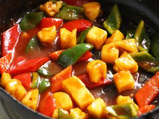 8、菠萝咕噜豆腐,锅内倒入适量油加热,倒入调味汁略炒一下,放入青红椒片和沥干盐水的菠萝块,翻炒片刻,使物料均匀裹上调味汁。