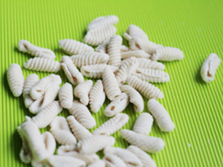 4、三鲜面蛹,放瓦楞纸上，用手指将面挤按扁的同时向前推动，使面团卷曲成蚕蛹形状的面蛹