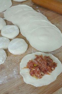 7、徐州过年头牌美食—猪肉饺子,将小面剂子挨个的按压扁，打圈擀成中间厚四周薄的饺子皮，皮中间放入适量的馅料。