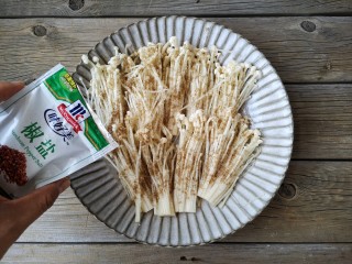 4、椒盐金针菇,将处理好的金针菇平铺在盘中，均匀撒上适量的椒盐，如果有时间可以腌制10分钟，没时间就接着进行下面的操作即可。
