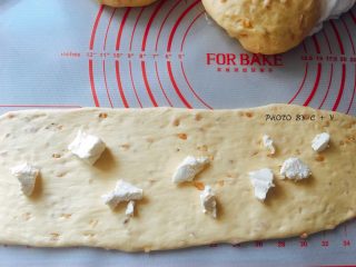 9、颗颗香浓花生粒入口的南瓜乳酪软欧包,依次将面团擀成长舌状，中间撒上散乱的奶油奶酪，由上往下卷起来。