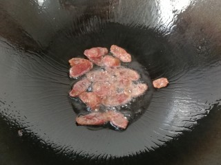 6、腊肠手撕包菜,锅中入少许油，下腊肠片煸香，煸至腊肠稍微出油；