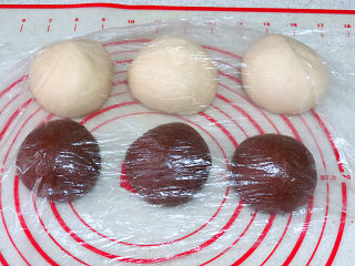 8、松软绵绵滴【可可双色面包】,发酵结束后，将面团取出排气，将两份面团各分割成3份，滚圆后放在案板上，盖保鲜膜松弛15分钟