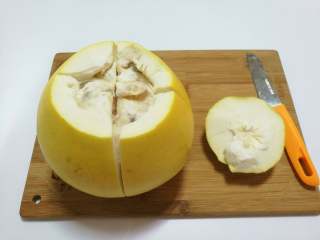 2、糖渍柚皮丝,削掉柚子顶尖部位，用刀将柚子划十字形，从上往下划开。