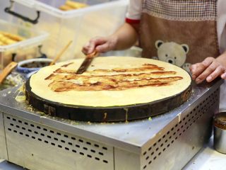 12、天津老味煎饼果子,这时小铲子登场，用小铲子轻轻松动煎饼边缘，双手一提一翻，煎饼就被反过来了，顿时能闻到煎饼的清香味，蛋香味，香葱味，在煎饼上抹上少许的天津甜面酱，腐乳酱汁和辣椒酱，煎饼上一道深褐色，一道浅粉色，一道酱红色，咸香甜俱全。