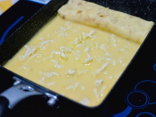 13、芝士肉松玉子烧,加热至蛋液底部开始凝固时，在表层均匀地撒上适量芝士碎。