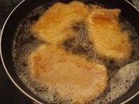 3、猪排丼,锅子里面加入足够油炸的油之后加热到180度左右,把猪排放进去炸至金黄后放到网架上沥干油分备用。(如果是直接吃炸猪排那就最好是炸两遍完全炸熟,但是做猪排丼的话就没关系,等会儿还要煮。)