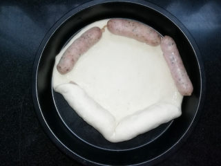 5、满园春色香肠披萨,用边缘的饼皮包裹住香肠。