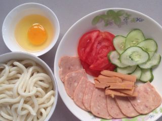 1、过桥乌冬面,备料：鸡蛋打出来整个，乌冬面沸水煮散沥干水份，挑出。切午餐肉肉薄片，黄瓜薄片，番茄薄片，玉米肠切条！备用。