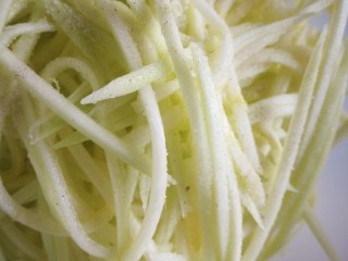 2、凉拌生瓜,生瓜用擦片器擦丝，加用一茶勺盐码五分钟，挤去水分，放大容器中备用。