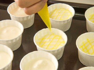 13、柠檬戚风小蛋糕,再取少量的柠檬酱也同时放入裱花袋里，剪小空，依次在蛋糕糊的表面画出网状纹路。这里剪的孔不要太大，避免画出来的线条过于粗糙不细致